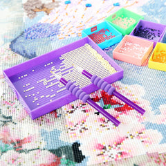 Diamond painting tool set in use, with two purple pens and a sorting tray filled with white drills – perfect for focused crafting at home.