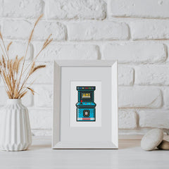 Framed diamond painting of a retro arcade machine design, placed on a modern white table with dried florals.