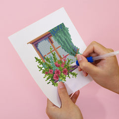 Hands placing resin drills onto soft canvas of floral window DIY diamond painting kit