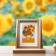 Framed diamond painting of sunflowers displayed on a wooden stand, with blurred sunflower background for vibrant home decor inspiration.