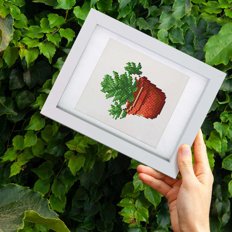 Hands holding framed plant diamond painting against garden backdrop – ideal for gift giving and nature lovers.