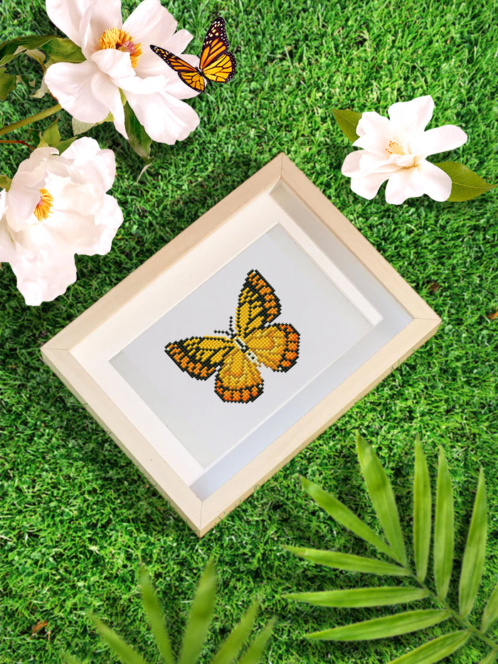 Framed yellow butterfly mini diamond painting displayed on grass with flowers – makes a bright and cheerful handmade gift.