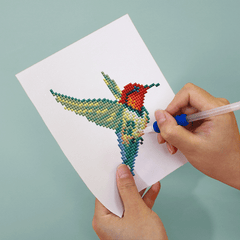 Hands placing resin drills on bird design canvas – diamond painting in progress.