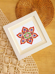 Red-pink mandala diamond art in white frame, styled on rattan placemat – boho interior inspiration.