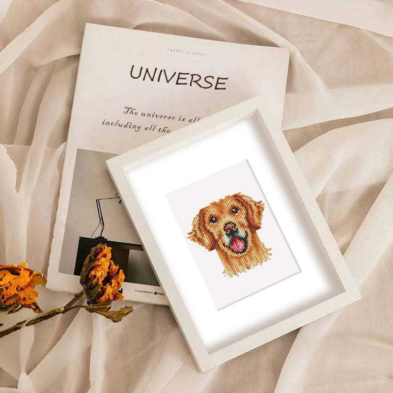 Framed diamond painting of a golden dog, resting on a fabric book for a cozy feel.