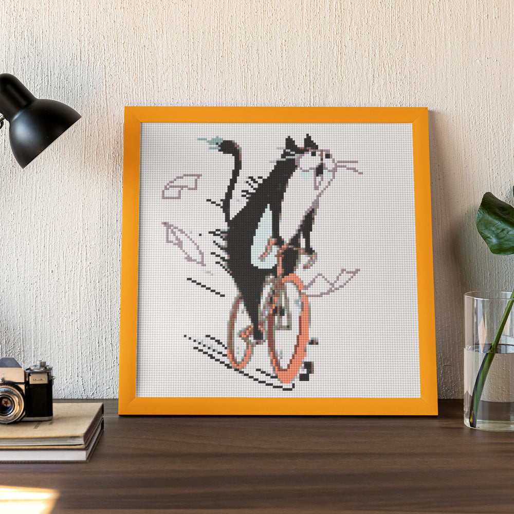 Framed small diamond painting of a funny cat on a bike, ideal for humorous desktop decoration or gifting.