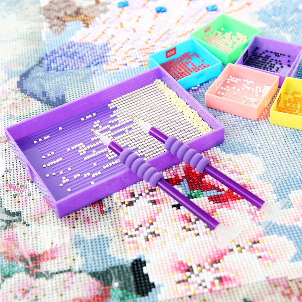 Diamond painting tool set in use, with two purple pens and a sorting tray filled with white drills – perfect for focused crafting at home.