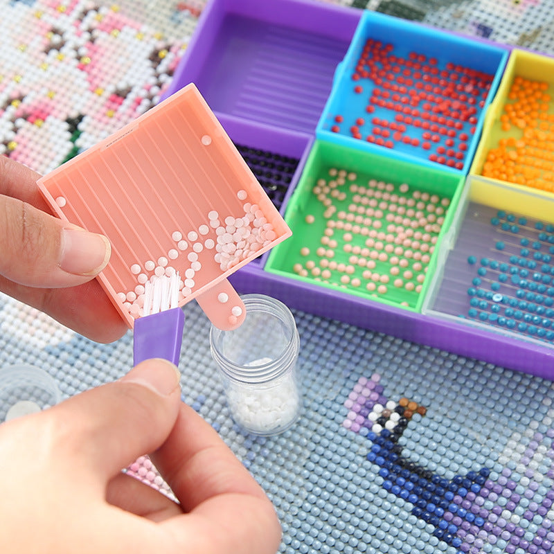 Hand using a brush to transfer white diamond drills from pink tray to jar – designed for neat, mess-free crafting and mindful hobbyists.