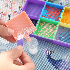 Hand using a brush to transfer white diamond drills from pink tray to jar – designed for neat, mess-free crafting and mindful hobbyists.