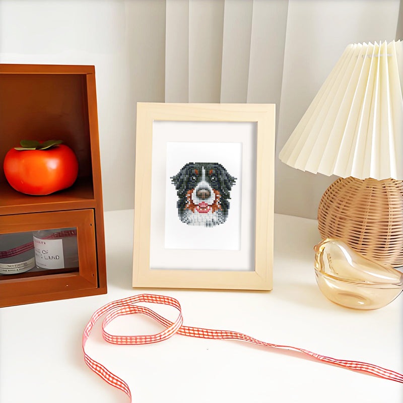 Diamond painting of a black dog in a white frame next to a warm-lit lamp.