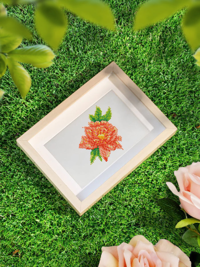 A small framed yellow-orange flower diamond art displayed on green grass, perfect for gifting or botanical wall decor.
