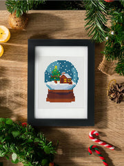 Diamond painting of Crystal Snowball with tree and presents, displayed on wood table with pine garland.
