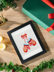Framed mini diamond painting of red and blue Christmas mittens tied with a bow, placed beside holiday gift box and candles – beginner-friendly holiday diamond art for cozy seasonal crafting.