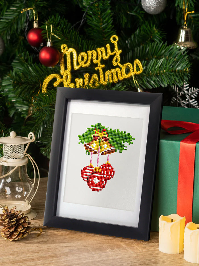 Finished diamond painting of red holiday bells framed and placed beside a Christmas tree. Ideal holiday wall art for entryways and mantelpieces.