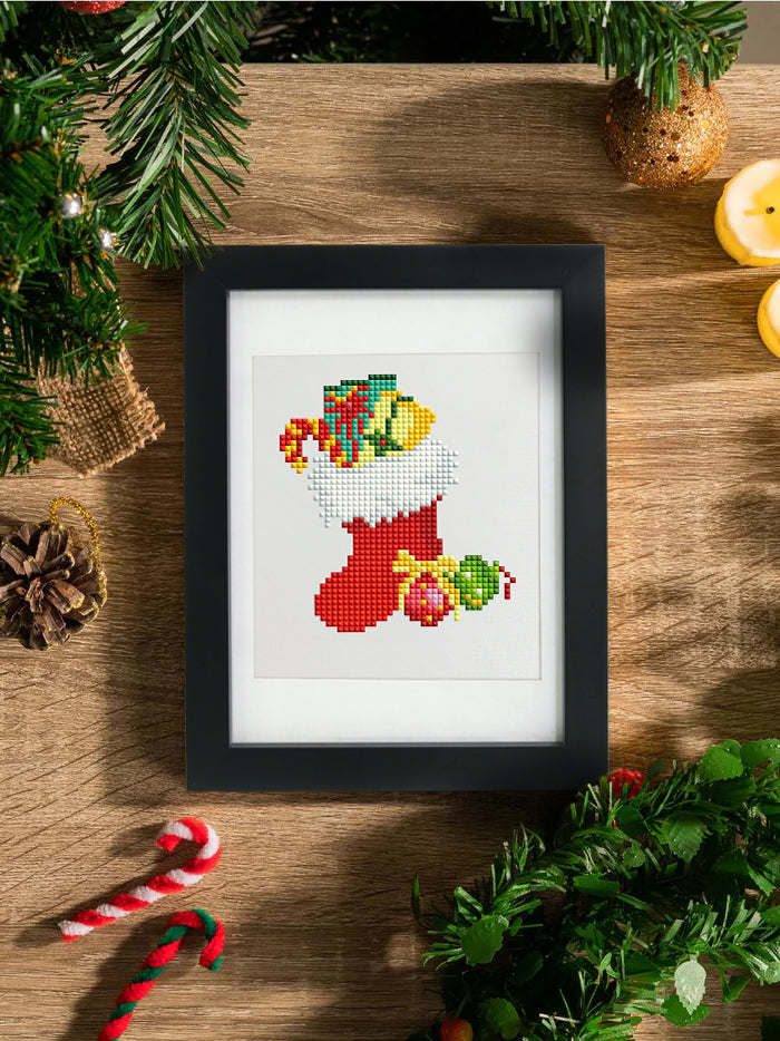Framed mini diamond painting of a red Christmas stocking filled with gifts, styled with pine branches and candy canes for festive home decor.