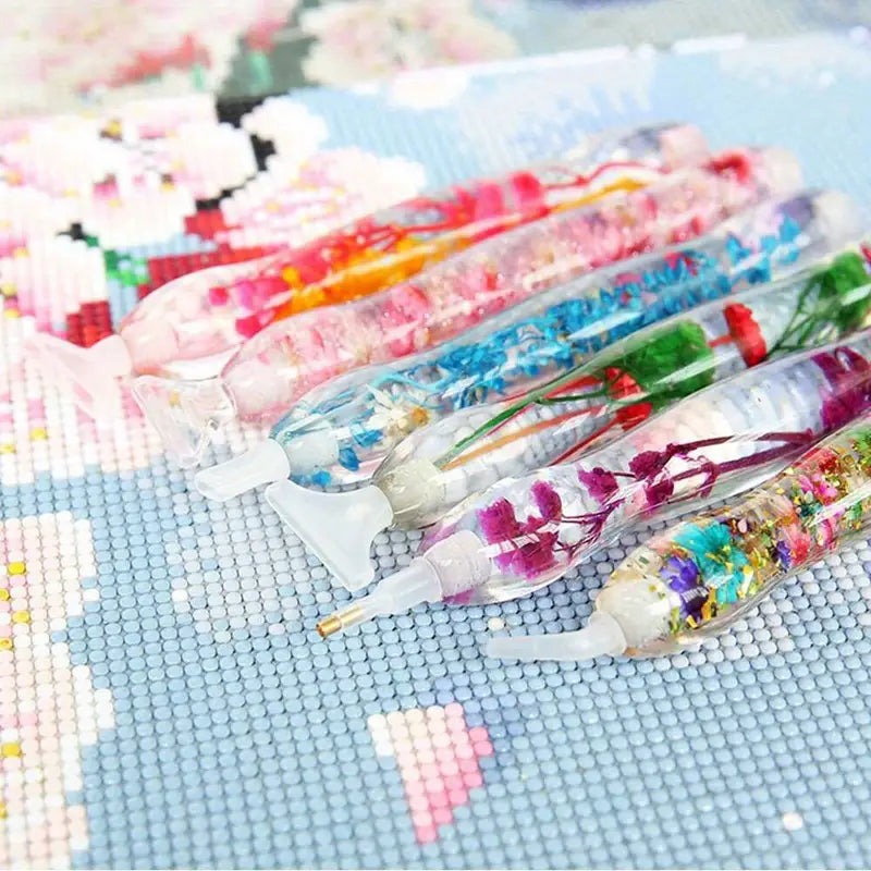 Diamond painting pens with real flowers styled on a floral background – perfect for artistic inspiration and gift displays.
