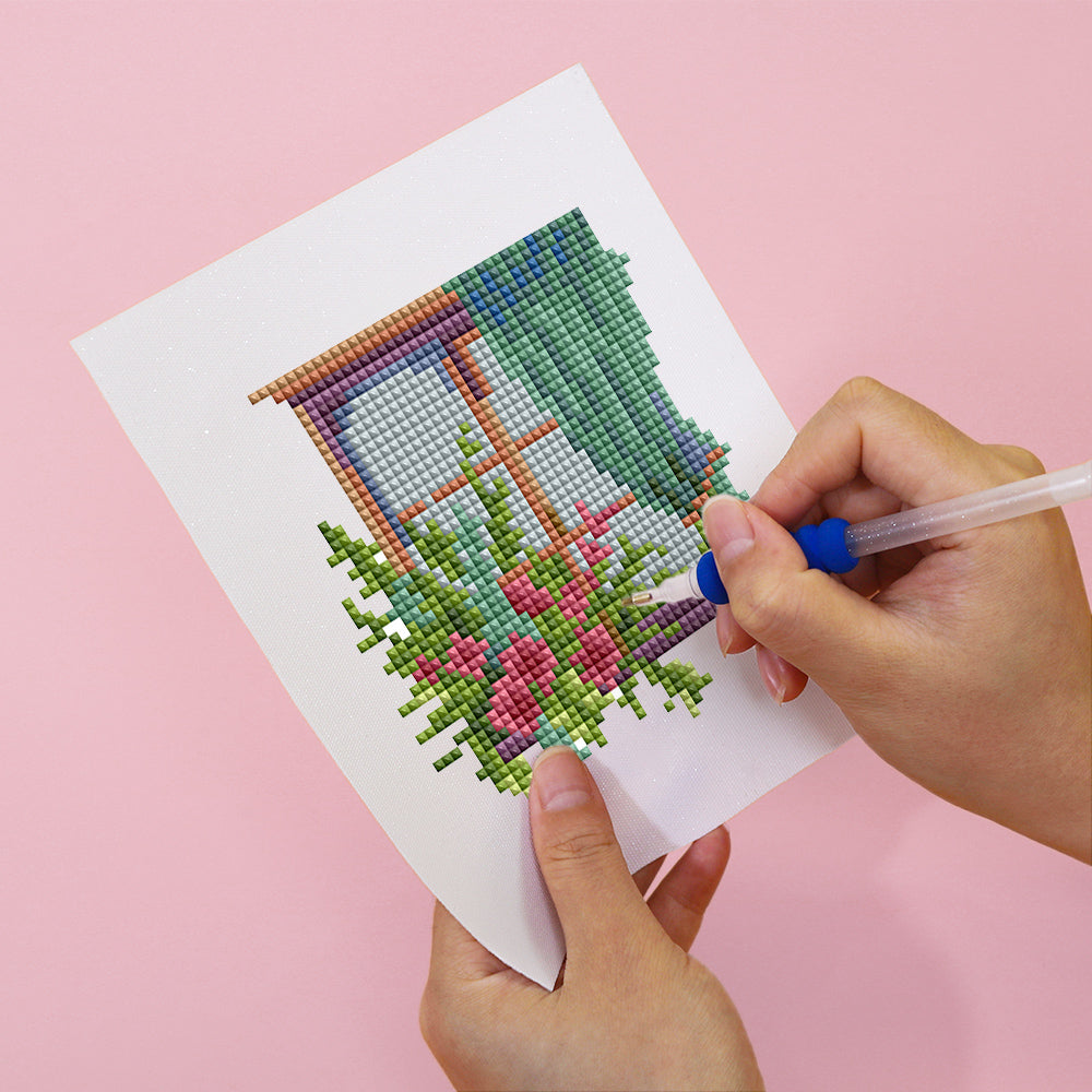 Hands placing resin drills onto soft canvas of floral window DIY diamond painting kit