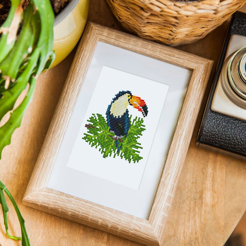 Finished bird diamond painting framed and displayed on a table with greenery.