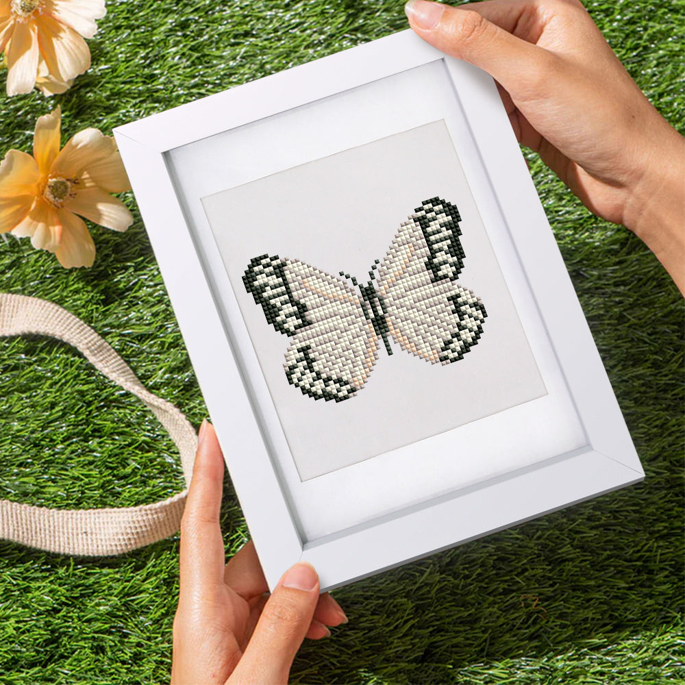 Close-up of hands holding a finished white and black butterfly diamond art piece outdoors – great for nature lovers and calm minds.