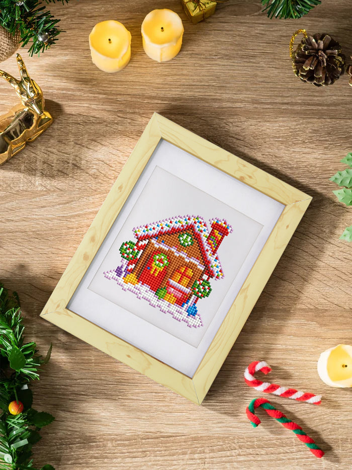 Diamond painting of a festive bell resting on a wood table with candles and greenery. Easy to make and great for seasonal DIY decoration.
