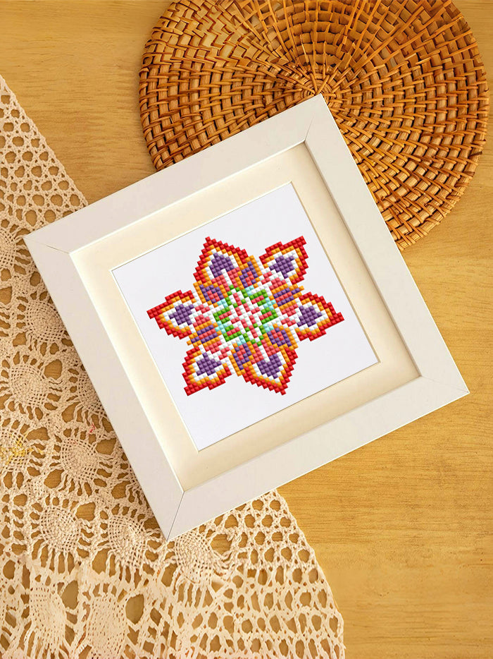 Red-pink mandala diamond art in white frame, styled on rattan placemat – boho interior inspiration.
