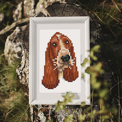 Framed diamond painting of a spaniel placed on outdoor rocks for rustic display.