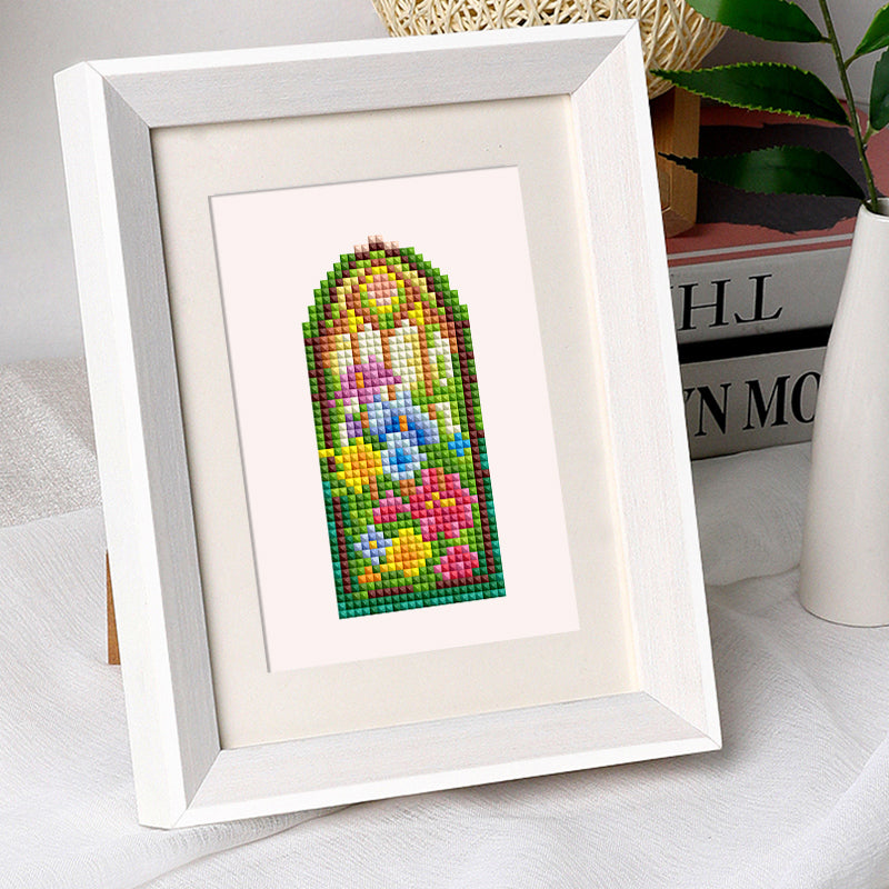 Finished stained glass diamond painting displayed on desk with books, showing vibrant arched window design. Perfect for relaxing craft time.