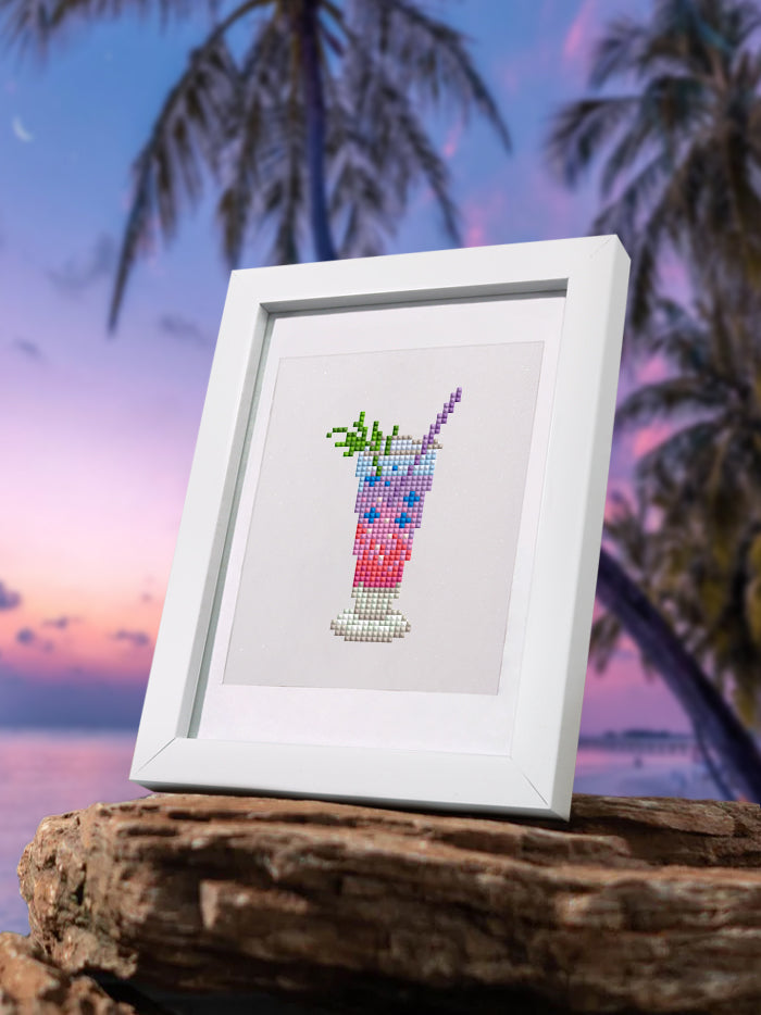 Finished pink drink diamond painting framed on driftwood with palm background – tropical home decor.
