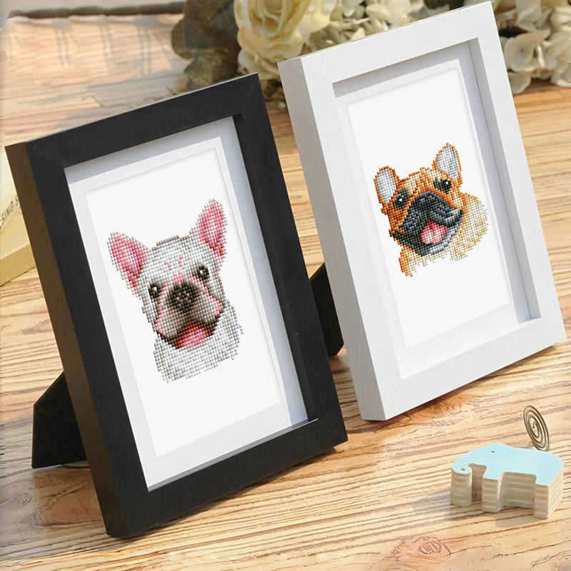 Two diamond paintings of dogs in white and black frames, set up on a wooden table.